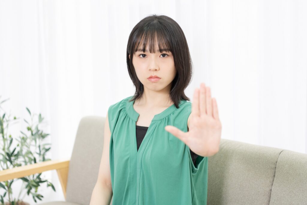 ソファに座ってNGのサインをする若い女性